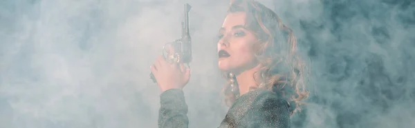 Panoramic shot of attractive woman holding gun near smoke — Stock Photo