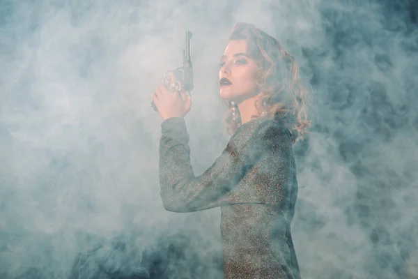 Femme attrayante et dangereuse tenant pistolet près de la fumée — Photo de stock