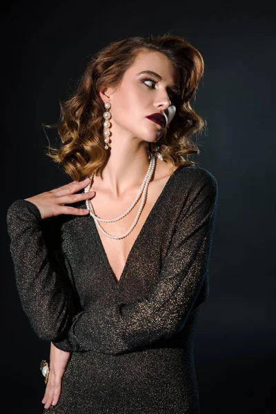 Atractiva mujer tocando collar de perlas en negro — Stock Photo
