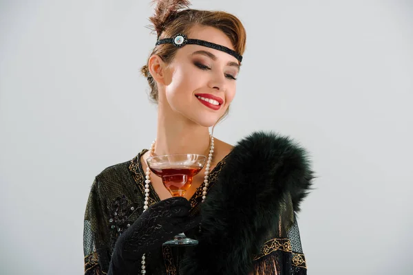 Cheerful aristocratic woman holding glass with drink isolated on grey — Stock Photo