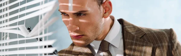 Panoramic shot of dangerous man touching window blinds with gun on white — Stock Photo