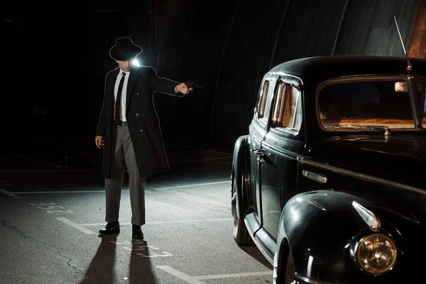 Красивий гангстер в капелюсі і пальто тримає пістолет біля ретро-автомобіля — стокове фото