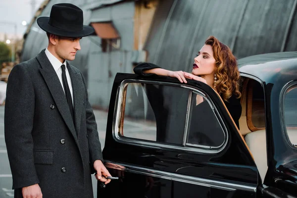 Hombre guapo en sombrero abriendo la puerta del coche cerca de mujer atractiva - foto de stock