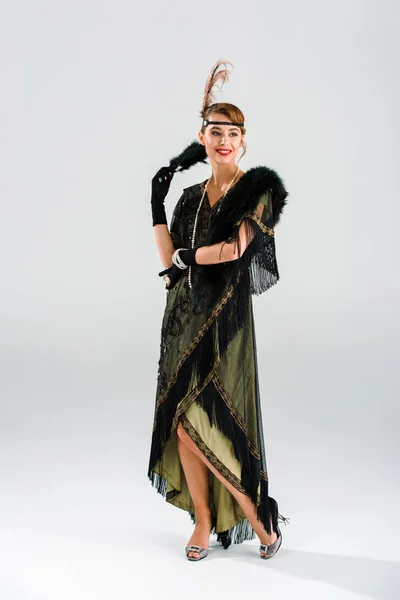 Веселая и аристократичная женщина держит перьевой веер на сером — стоковое фото