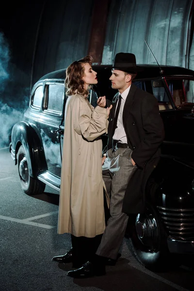 Beautiful woman standing near handsome gangster and retro car — Stock Photo