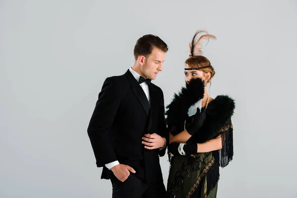 Bel homme debout avec la main dans la poche et regardant femme avec ventilateur de plumes isolé sur gris — Photo de stock