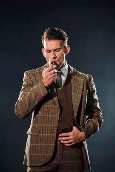 Handsome gangster in suit smoking cigar on black — Stock Photo