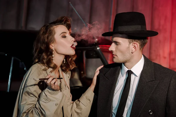 Attractive woman smoking cigarette near handsome gangster in hat — Stock Photo