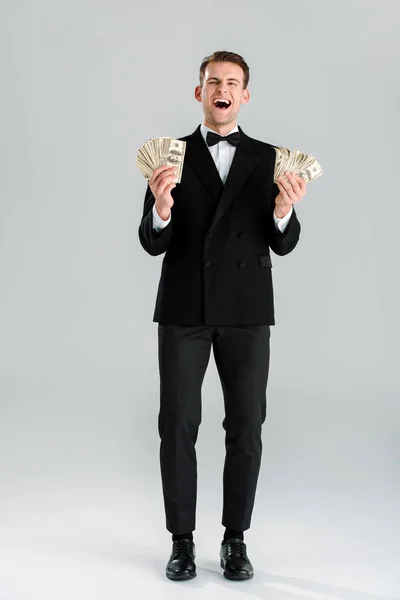 Glücklicher Mann im Anzug mit Dollarnoten auf grau — Stockfoto