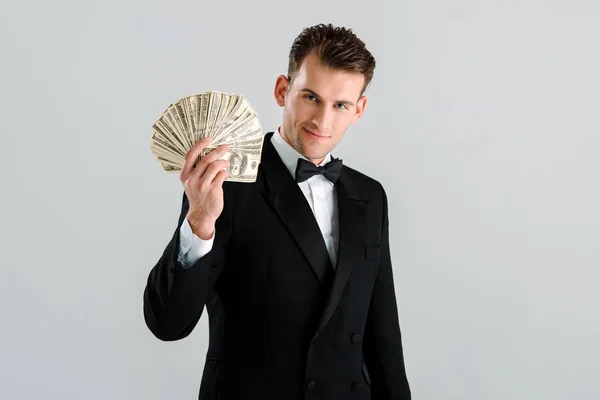 Happy and rich man in suit holding dollar banknotes isolated on grey — Stock Photo