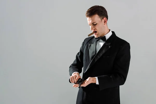 Dangerous gangster in suit with bow tie holding gun while smoking cigar isolated on grey — Stock Photo