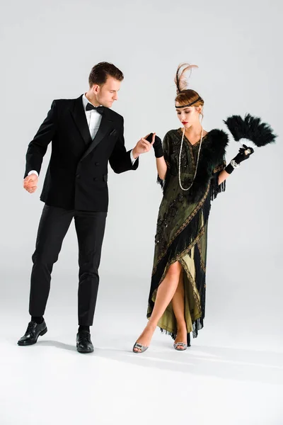 Elegante hombre de traje y mujer tomados de la mano mientras bailan en gris - foto de stock