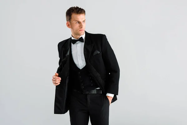 Stilvoller Mann in Anzug und Fliege stehend mit der Hand in der Tasche isoliert auf grau — Stockfoto
