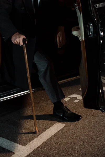 Vista recortada de gángster sosteniendo bastón cerca de coche retro con puerta de coche abierta - foto de stock