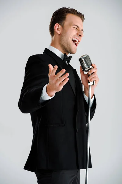 Hombre guapo cantando mientras toca micrófono aislado en gris - foto de stock