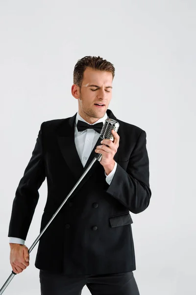 Hombre guapo en traje tocando micrófono retro mientras canta aislado en blanco - foto de stock