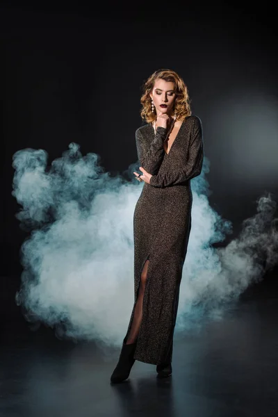Attractive woman in dress standing on black with smoke — Stock Photo