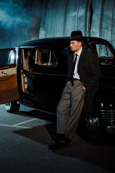 Gangster bonito em chapéu de pé com as mãos no bolso perto do carro — Fotografia de Stock