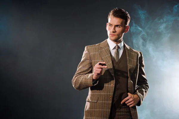 Handsome and rich man in suit holding cigar on black with smoke — Stock Photo