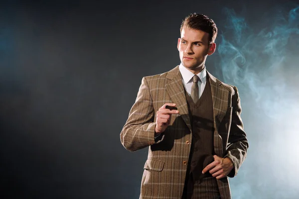 Bel homme riche en costume tenant cigare sur noir avec de la fumée — Photo de stock