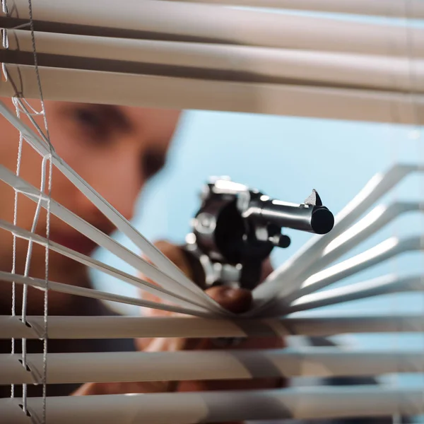 Foco seletivo de arma preta perto de persianas de janela na mão de gangster — Fotografia de Stock