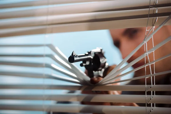 Disparo panorámico de arma negra cerca de persianas de ventana en mano de gángster - foto de stock