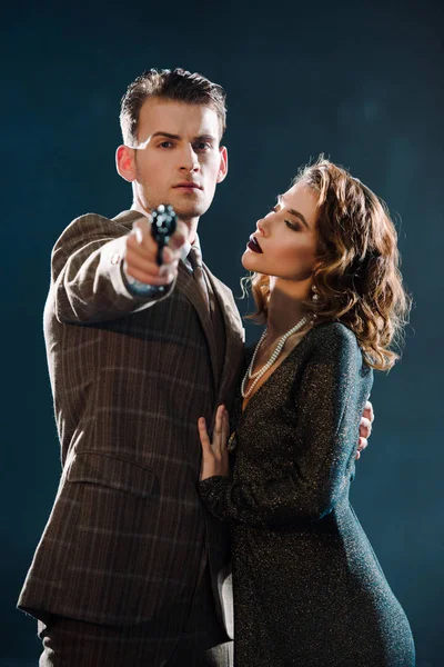 Selective focus of dangerous man holding gun and looking at camera near attractive girl on black — Stock Photo