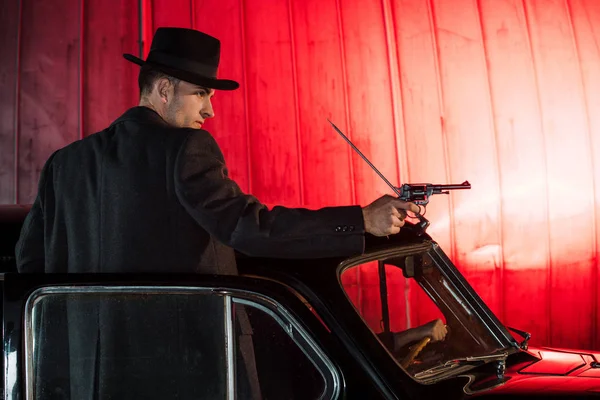 Красивий гангстер тримає пістолет, стоячи біля старовинної машини — стокове фото