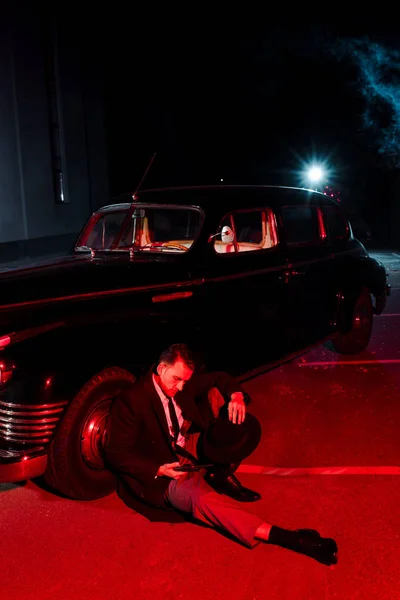 Handsome gangster sitting near car and looking at gun — Stock Photo