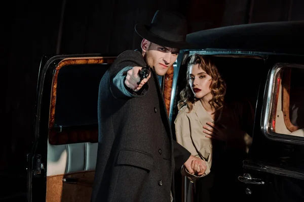 Selective focus of dangerous man holding gun near woman in retro car — Stock Photo