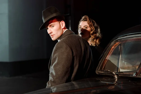 Bel homme en chapeau et manteau debout près de la femme et voiture rétro — Photo de stock