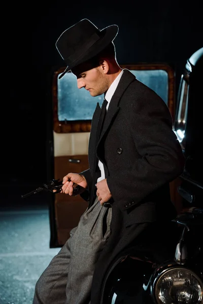 Вид сбоку на красивого человека в шляпе, держащего пистолет рядом с винтажной машиной — стоковое фото