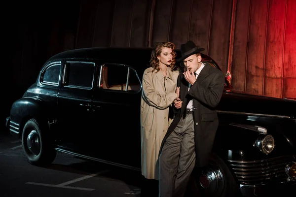 Handsome man in hat smoking cigar near attractive woman and vintage car — Stock Photo