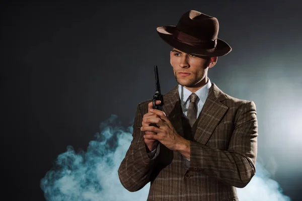 Bonito homem no siot e chapéu segurando arma no preto com fumaça — Fotografia de Stock
