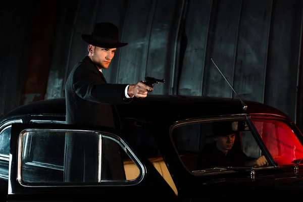 Hombre peligroso en sombrero sosteniendo pistola cerca de coche retro — Stock Photo