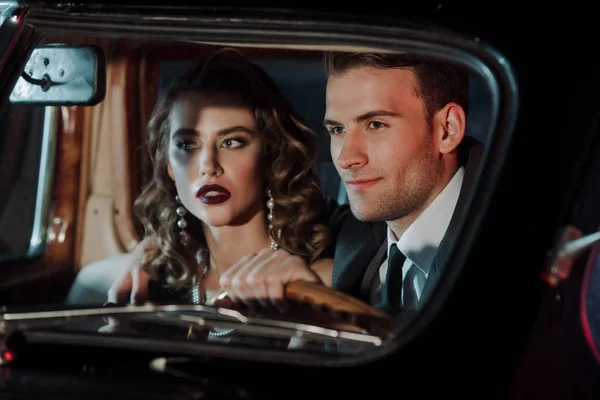 Selective focus of happy man touching steering wheel and sitting near attractive woman in retro car — Stock Photo