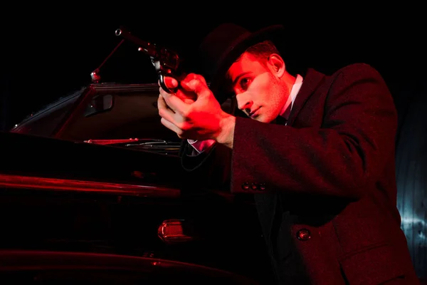 Selective focus of dangerous man holding gun near retro car on black — Stock Photo