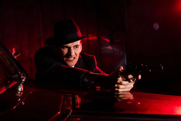 Gángster enojado en sombrero sosteniendo pistola cerca de coche retro - foto de stock