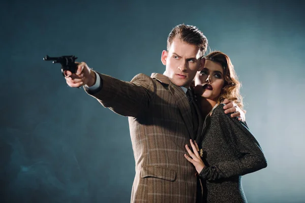 Selective focus of dangerous man holding black gun near woman on grey — Stock Photo