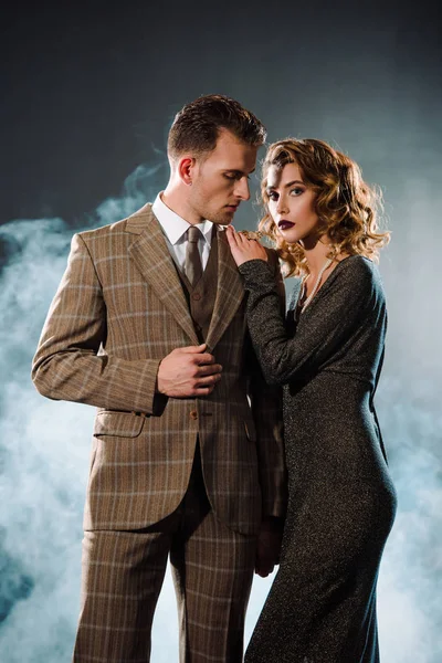 Attractive woman standing with handsome gangster on black with smoke — Stock Photo