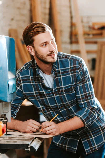 Selective focus of bearded carpenter holding pencil in workshop — Stock Photo