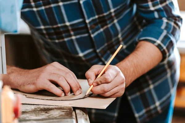 Cropped view of carpenter drawing while holding pencil in workshop — Stock Photo