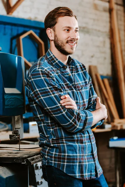 Cheerful carpenter standing with crossed arms in workshop — Stock Photo