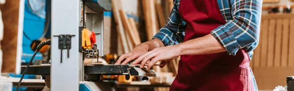 Panoramic shot of carpenter in apron using electric woodworking — Stock Photo