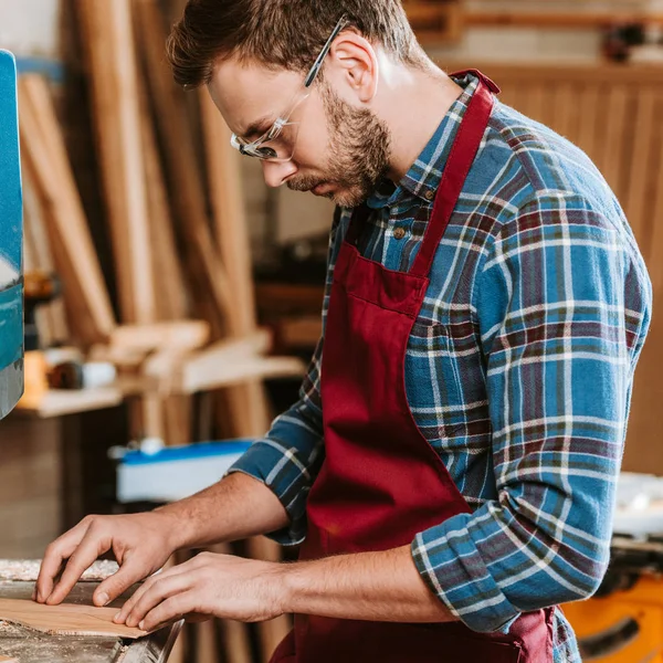 Bearded carpenter in protective glasses and apron in workshop — Stock Photo