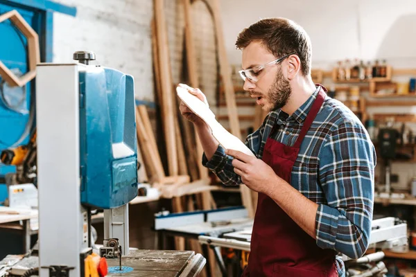 Selective focus of surprised carpenter looking at wooden cutting board — Stock Photo