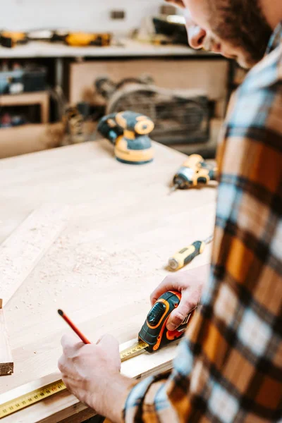 Cropped view of bearded carpenter measuring wooden plank — Stock Photo