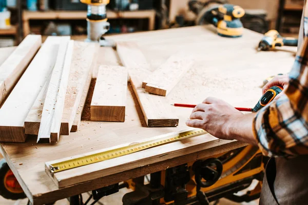 Cropped view of carpenter measuring wooden plank — Stock Photo