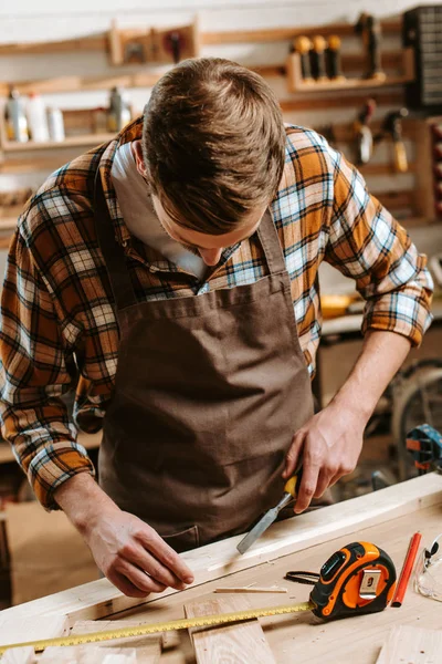 Carpenter carving wood near measuring tape in workshop — Stock Photo