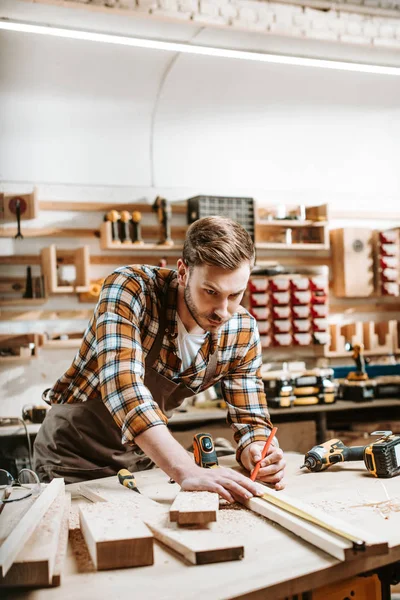 Selective focus of bearded woodworker measuring wooden plank — Stock Photo